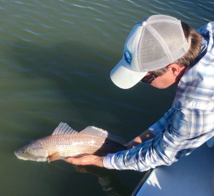 image of man holding fish off the side of a boat